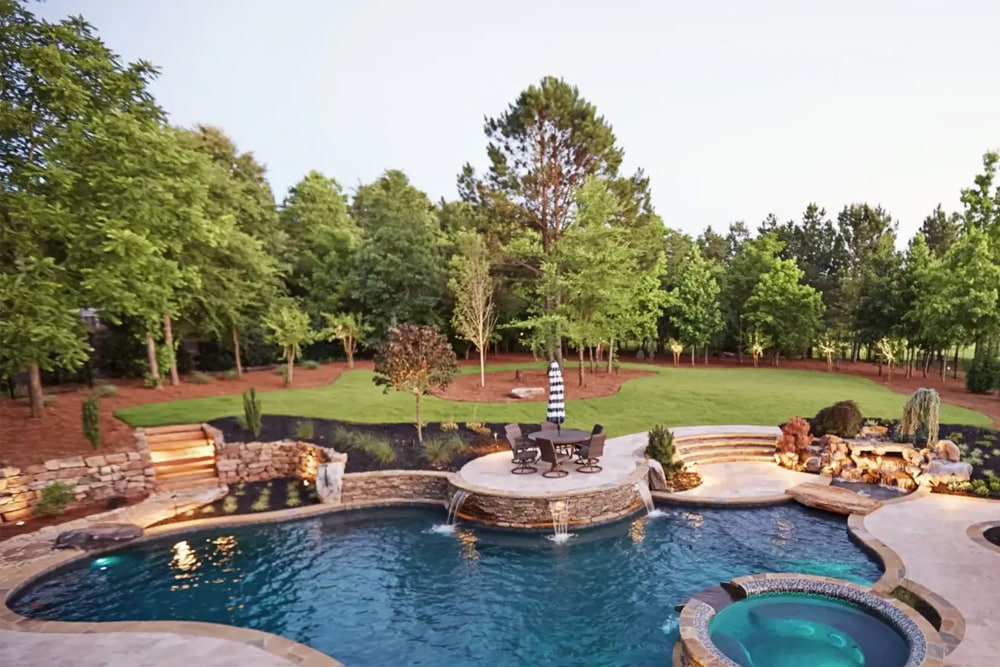 Luxury backyard featuring a pool, hot tub, patio seating, stone accents, lush green lawn, and tall trees in the background—an inviting oasis that showcases the meticulous care often achieved through expert Commercial Restoration Services.