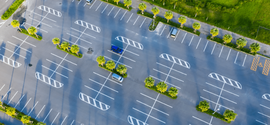 Aerial view of a mostly empty parking lot with a few parked cars and evenly spaced palm trees lining the rows, showcasing an ideal site for Commercial Restoration Services to enhance and maintain the property’s curb appeal.